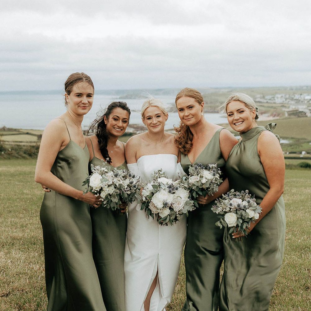Bride stands with her bridesmaids wearing green satin bridesmaid dresses with differing styles