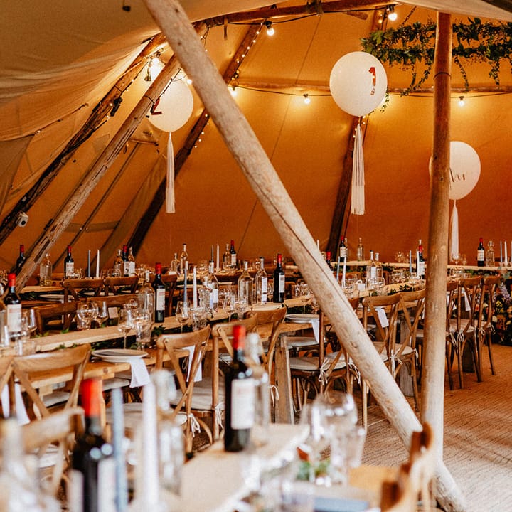 Tipi wedding reception with the pink neon sign and white balloon and tassel wedding table number signs with gin stations 