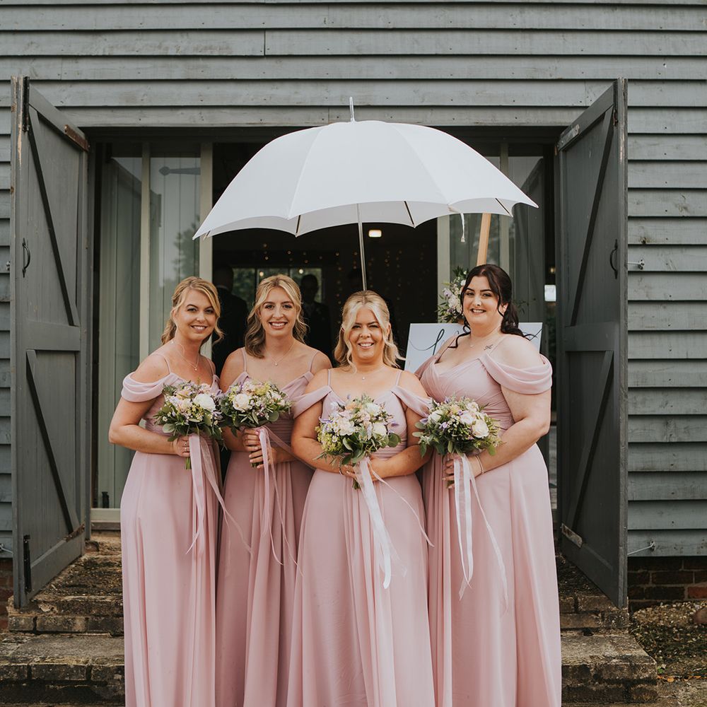 Bridesmaids in matching off the shoulder pink bridesmaid dresses under an umbrella 