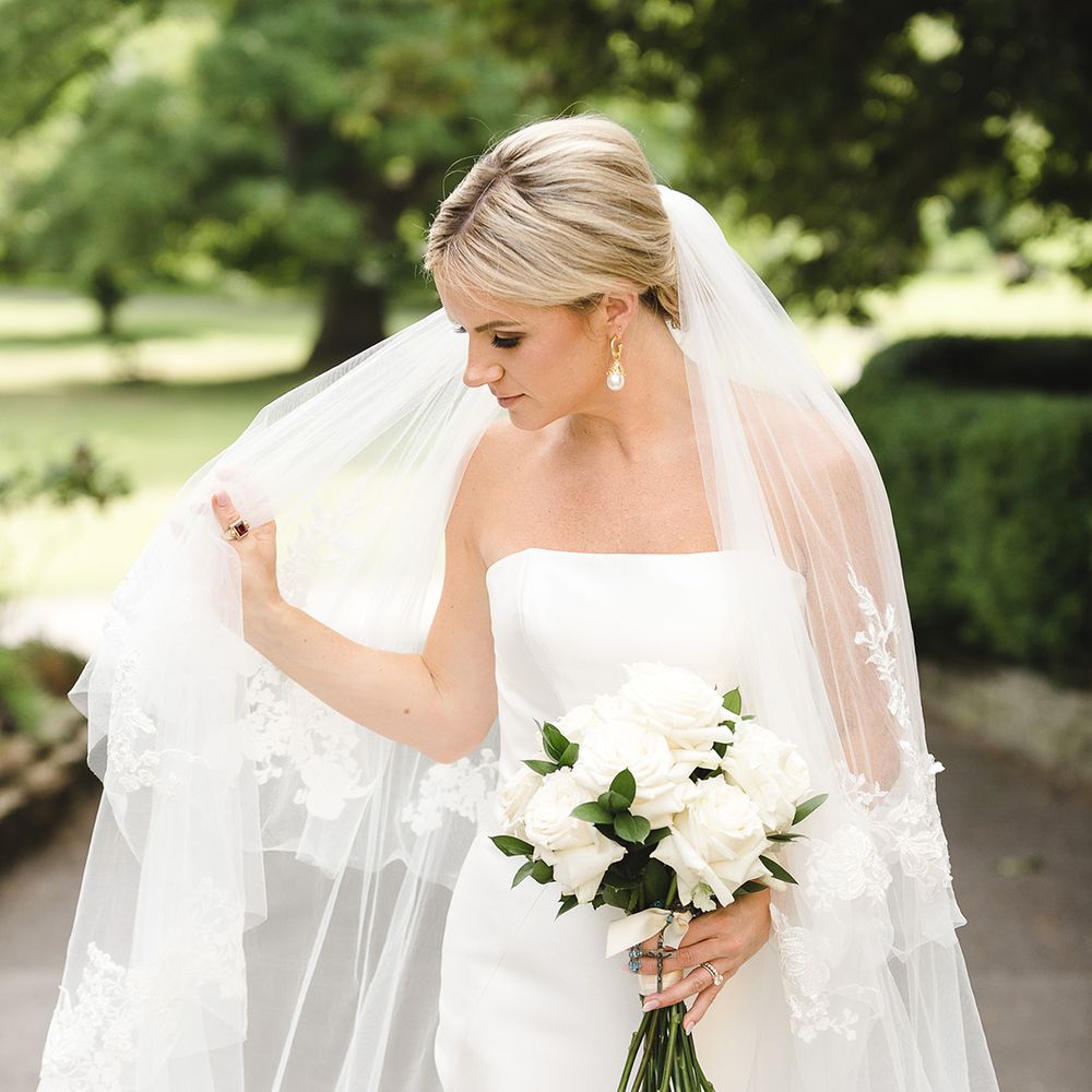 Bride in fitted mermaid wedding dress from Pronovias with embroidered veil holding classic white rose bouquet 