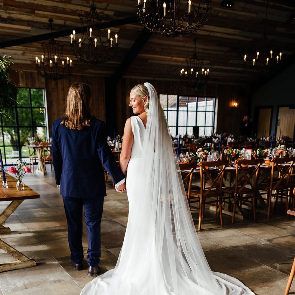 Bride wearing a fitted draped back wedding dress with long train and veil walking around the wedding reception 