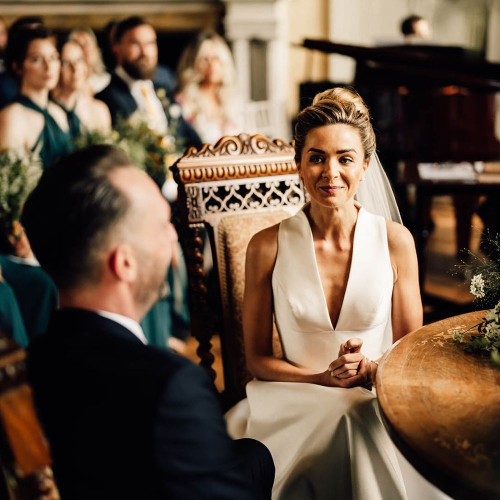 Bride in Sheila Harding wedding dress sits to sign the wedding register with the groom 