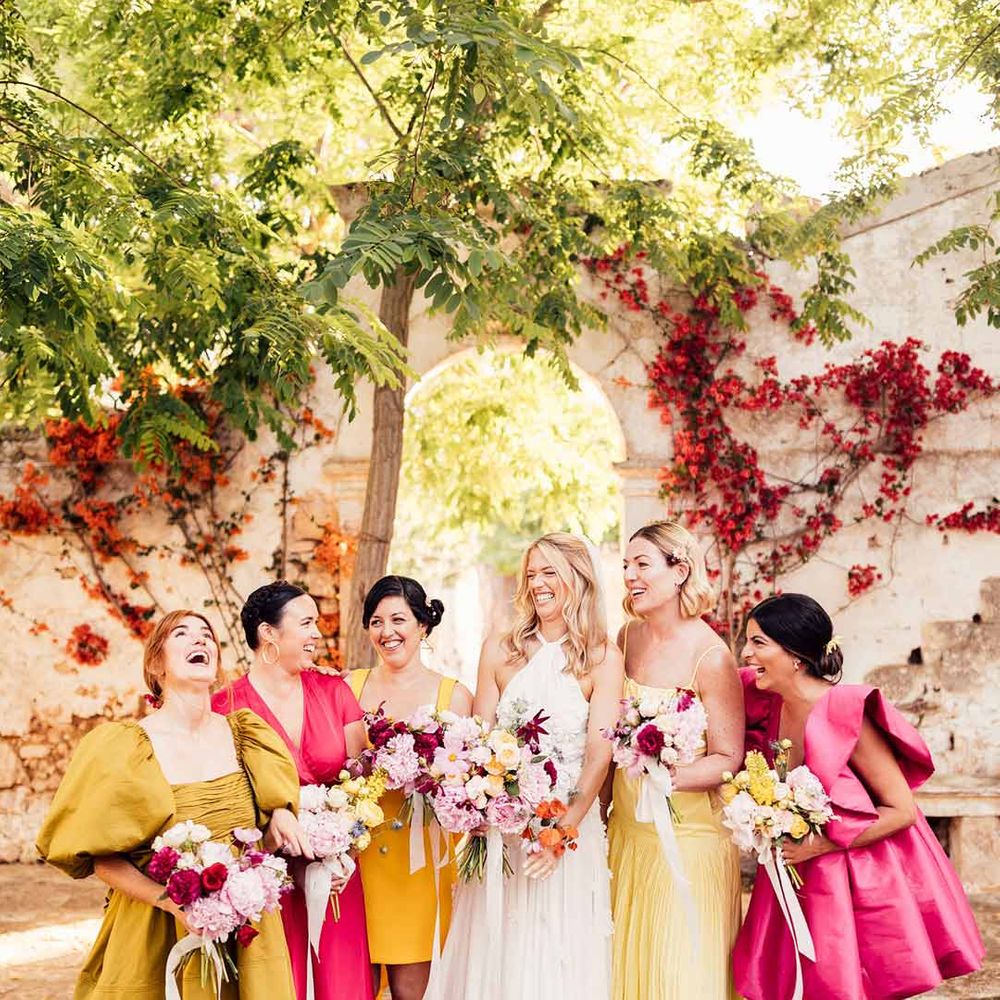 Bride wearing halterneck wedding dress standing with bridesmaids in vibrant mismatched bridesmaid dresses - hen party ideas