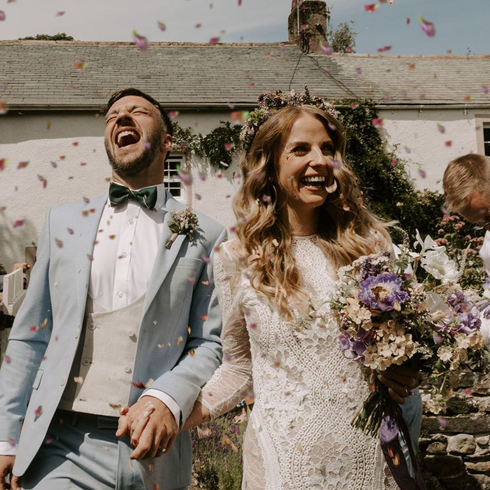 Bride in long sleeve high neck boho lace wedding dress having confetti exit with groom in pale baby blue three piece suit 