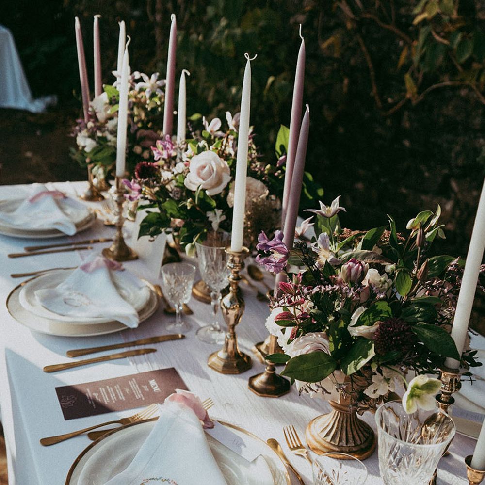 Purple and white taper candles with gold rimmed plates, gold cutlery, and crystal glassware 