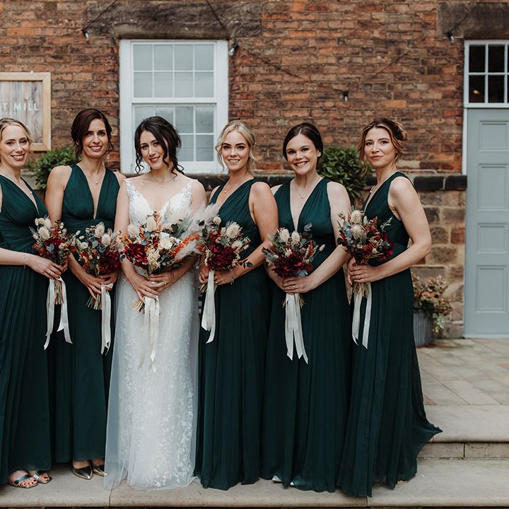 Bridesmaids wearing dark green bridesmaid dresses carrying bouquets tied with white ribbons for autumn wedding 