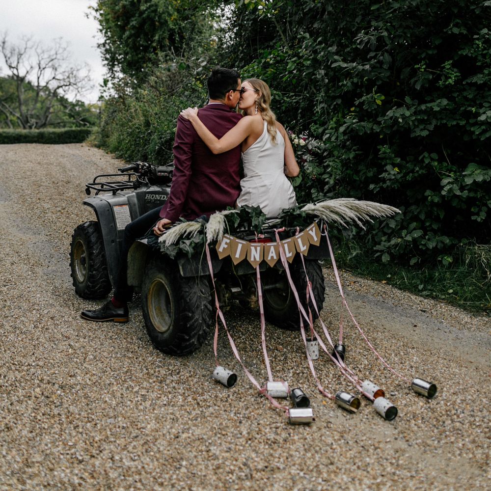 Bride and groom riding a quad bike with tin cans trailing