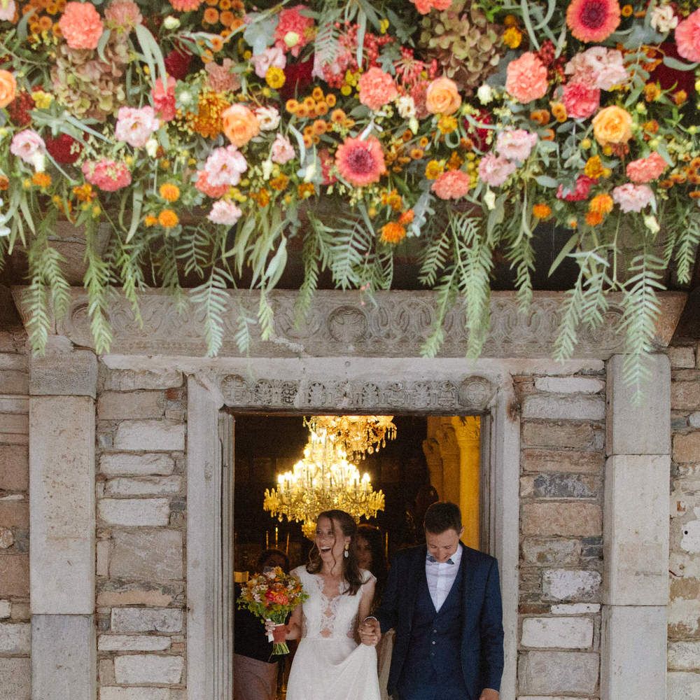The bride and groom exiting a stone doorway under a display of flowers