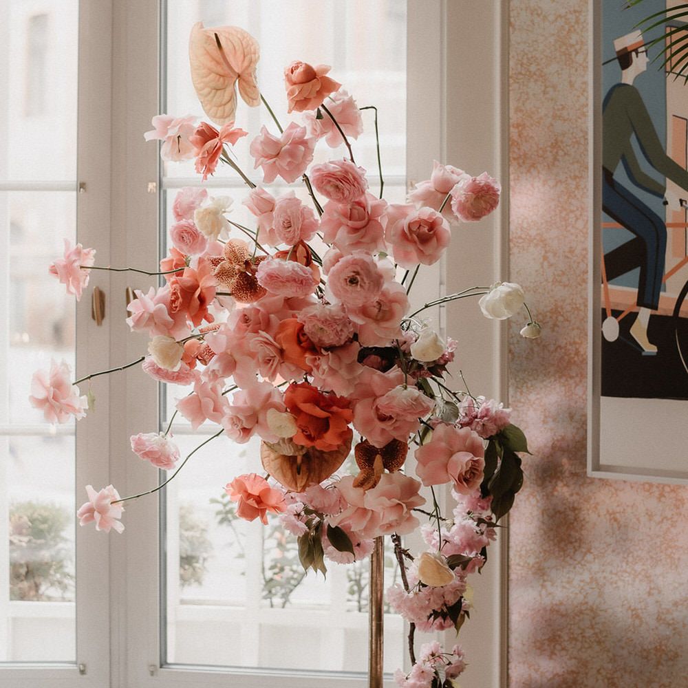 Standing pink floral display including pink, peach and burgundy ranunculi, garden roses and orchids
