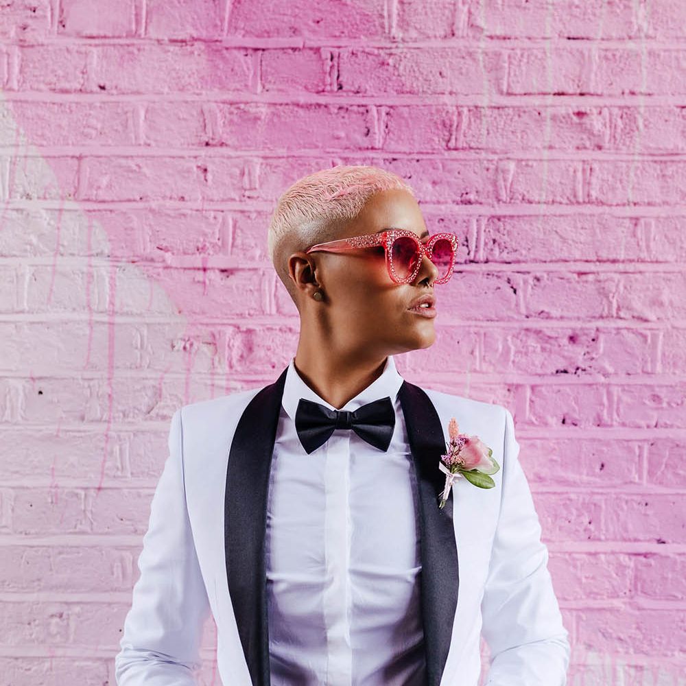 Stylish bride with short hair in a white tuxedo jacket and bow tie with pink sun glasses 