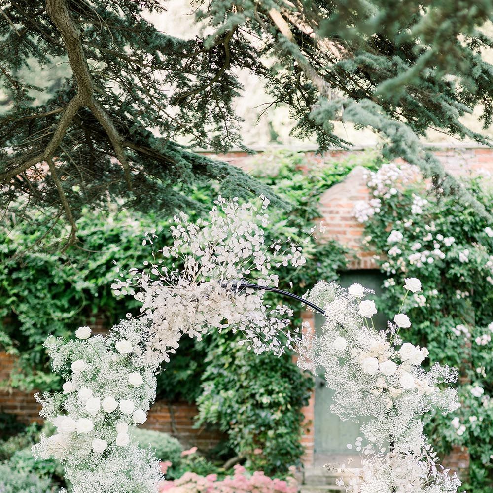 Outdoor ceremony at Garthymyl Hall wedding venue with white chairs and flower arch 