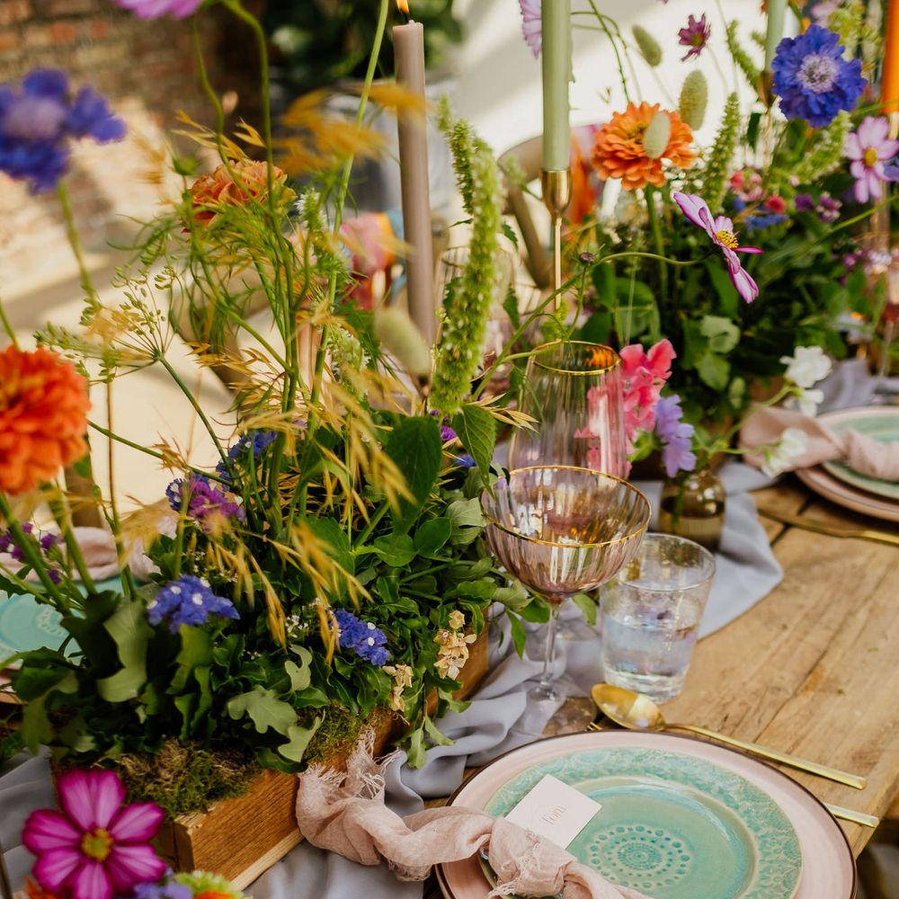 Place setting with pink and green tableware, table linen, wildflower centrepiece decor and iridescent glassware