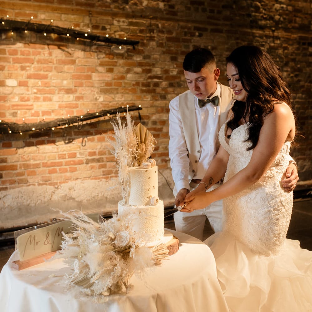 Bride and groom cutting their rustic wedding cake with dried flower decor and intricate design 