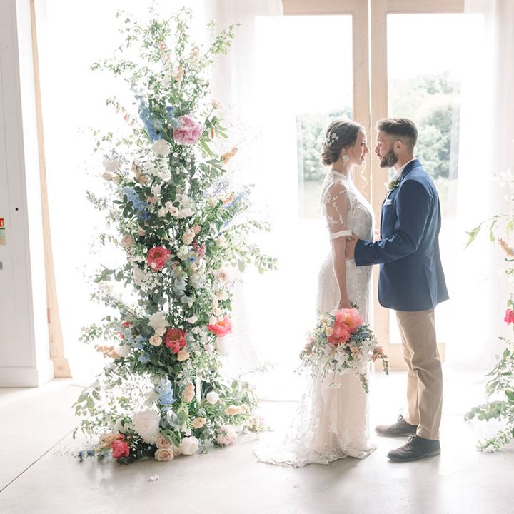 Bride and groom standing in the middle of pastel coloured vertical flower arrangements 
