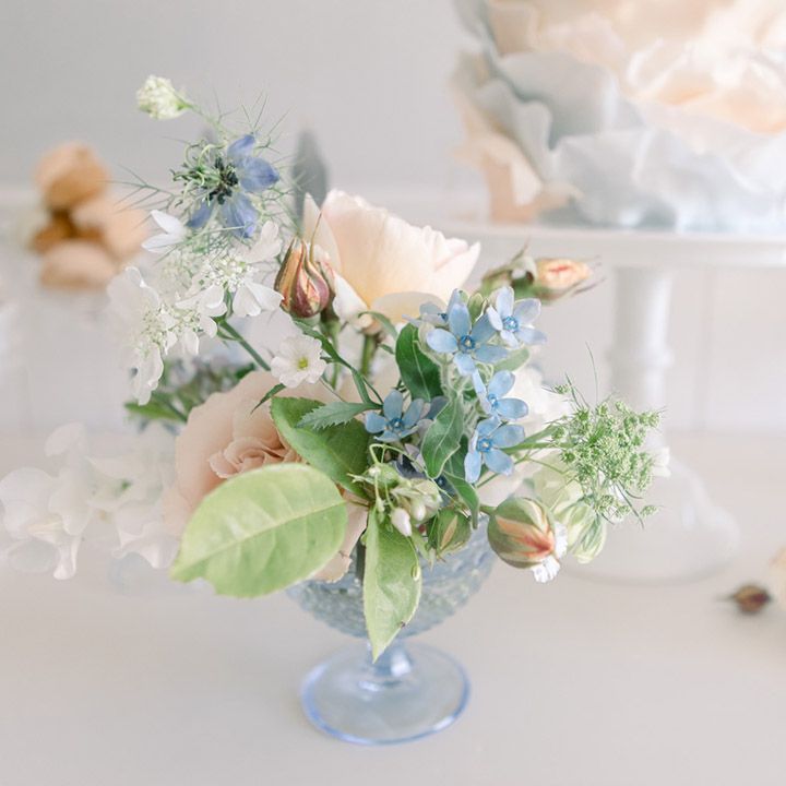 Small flower arrangement in a coloured glass vessel with peach roses and foliage 