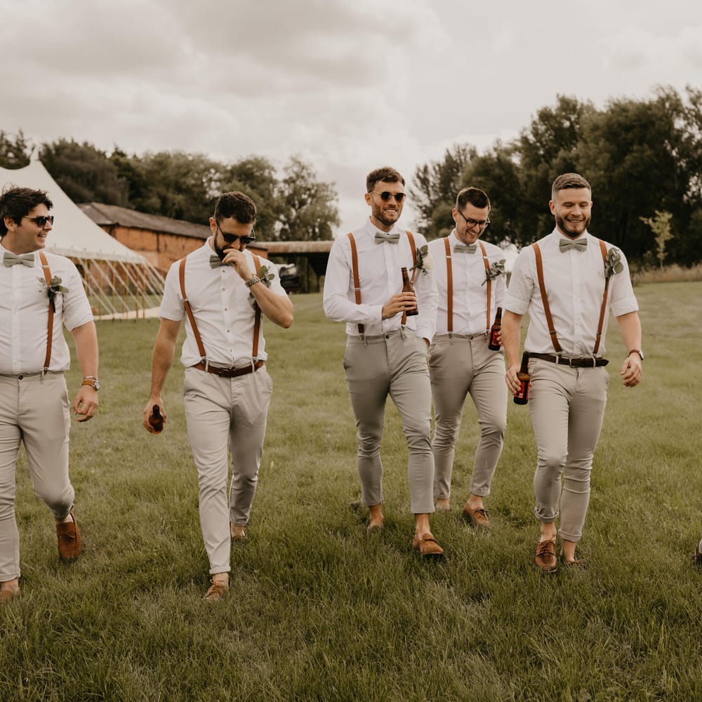 Groom and his groomsmen walk across field on his wedding day at Duddon Mill Farm | Mark Bamforth Photography