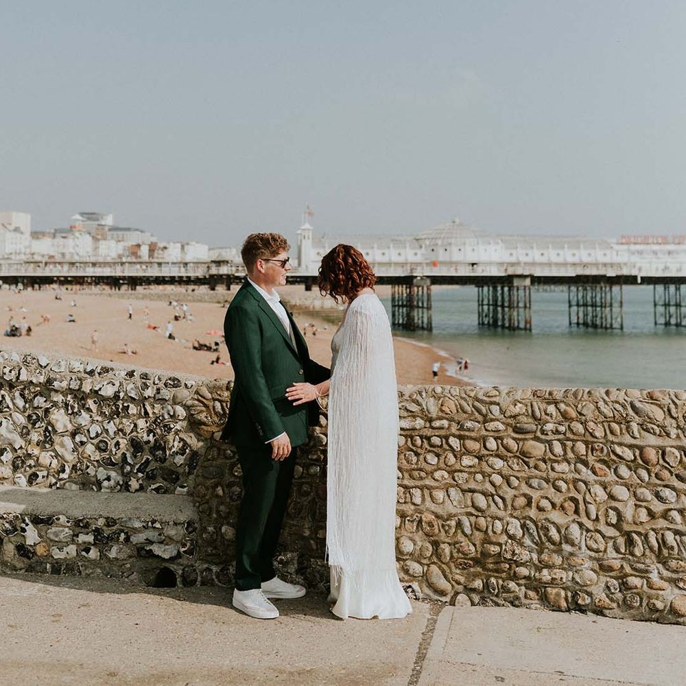 Bride & groom stand beside brick wall by the seaside beach front in Brighton on their wedding day