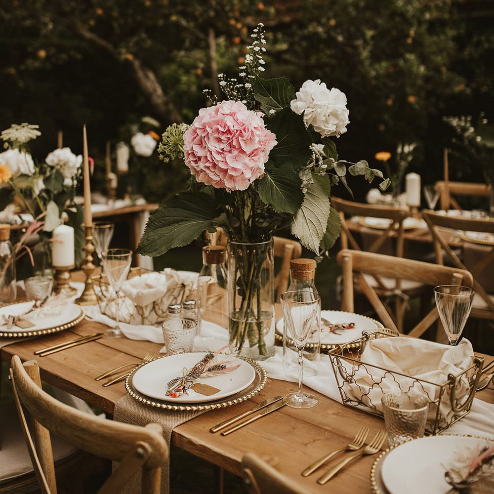 Rustic tablescape complete with wooden tables, large florals in pink and white and china plates