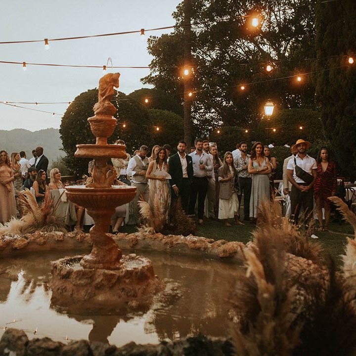 Wedding guests gather outdoors in front of fountain