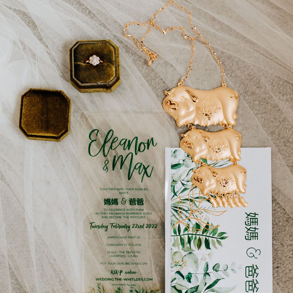 Transparent wedding invitation next to traditional gold Chinese jewellery and flower shaped diamond wedding ring
