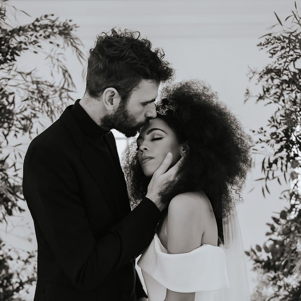 Black and white portrait of the groom kissing his brides forehead with naturally curly afro hair at Core Clapton Events London minimalist wedding venue 