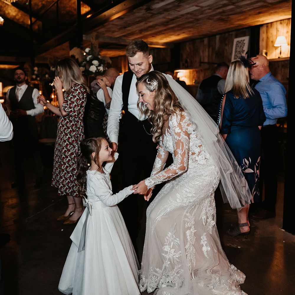 Bride in lace dress and moon and star hair accessories dances with flower girl as groom watches