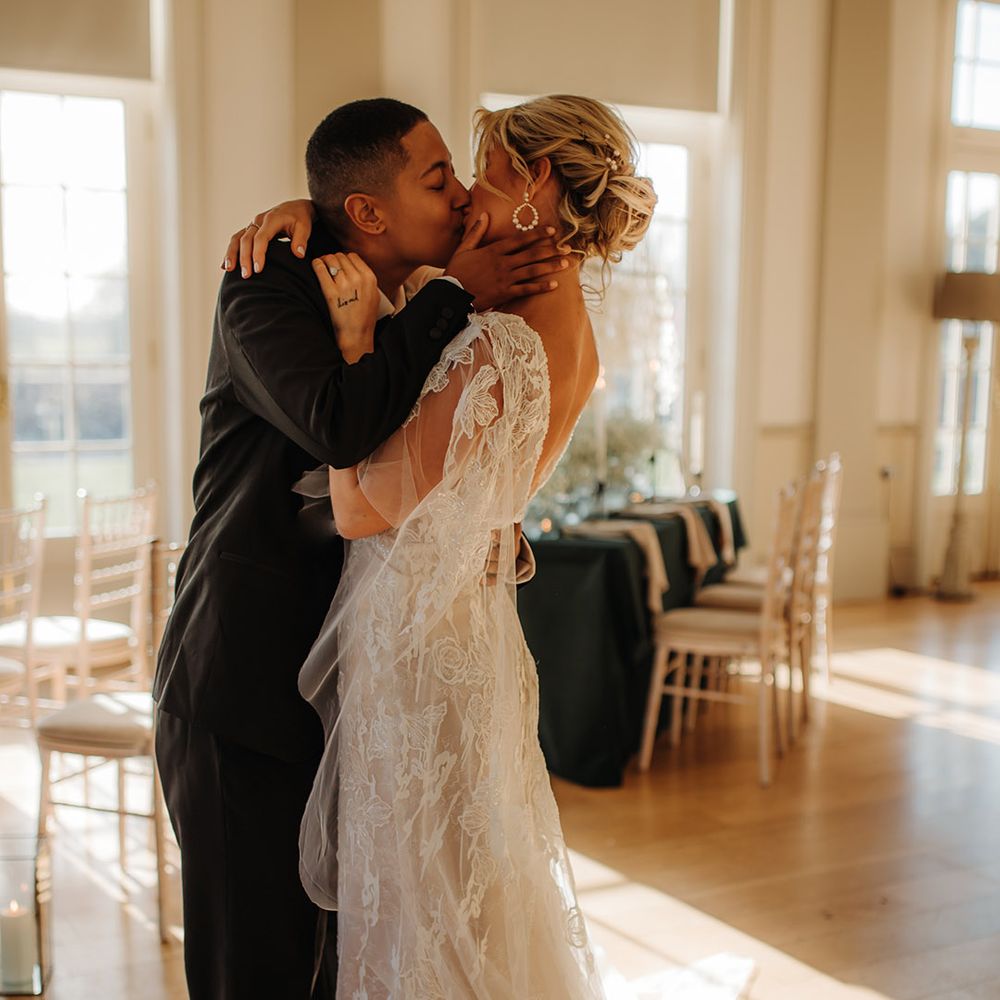 LGBTQI+ couple kissing wearing a black suit and applique wedding dress 