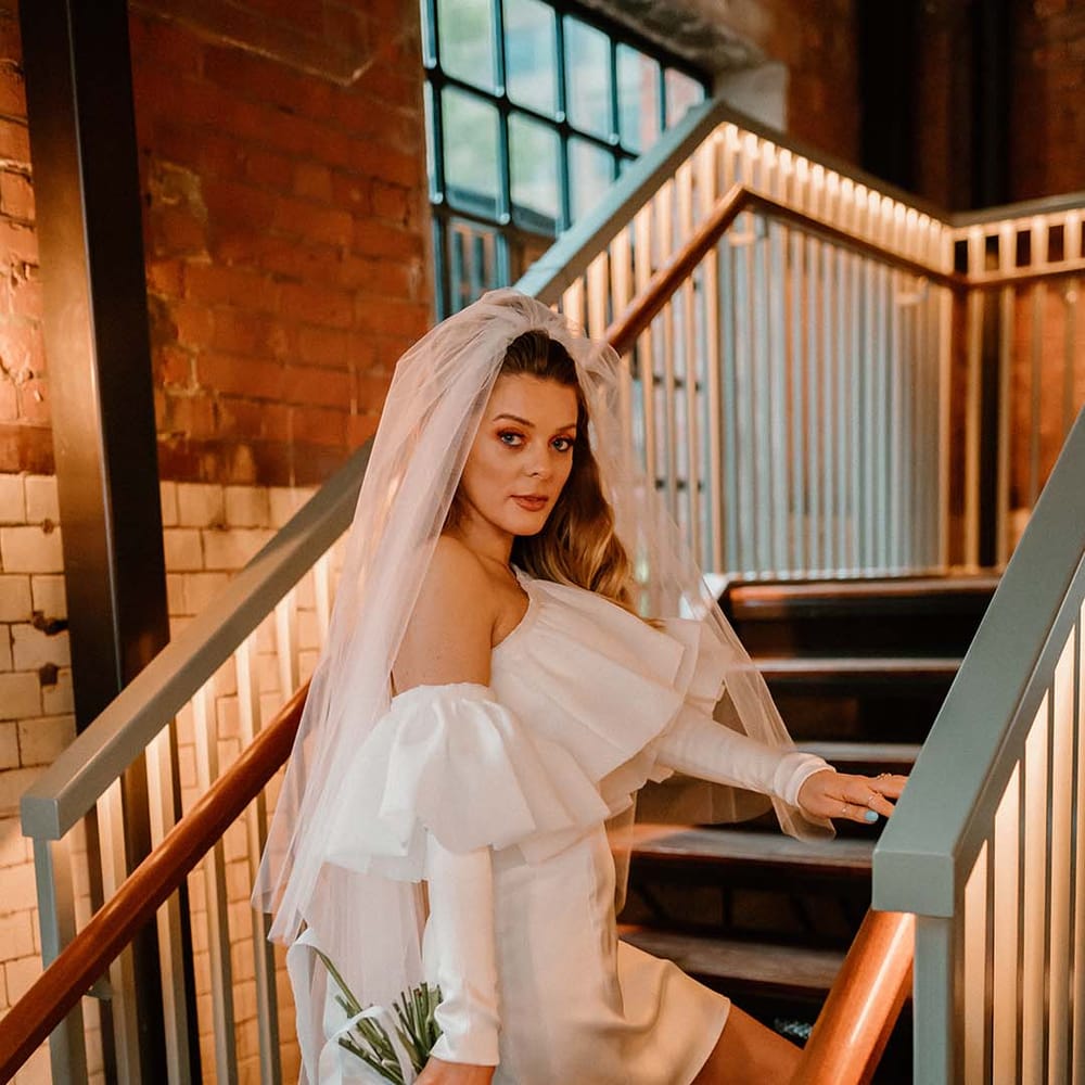 Stylish bride in an off the shoulder short wedding dress with detachable long sleeves and long wedding veil 