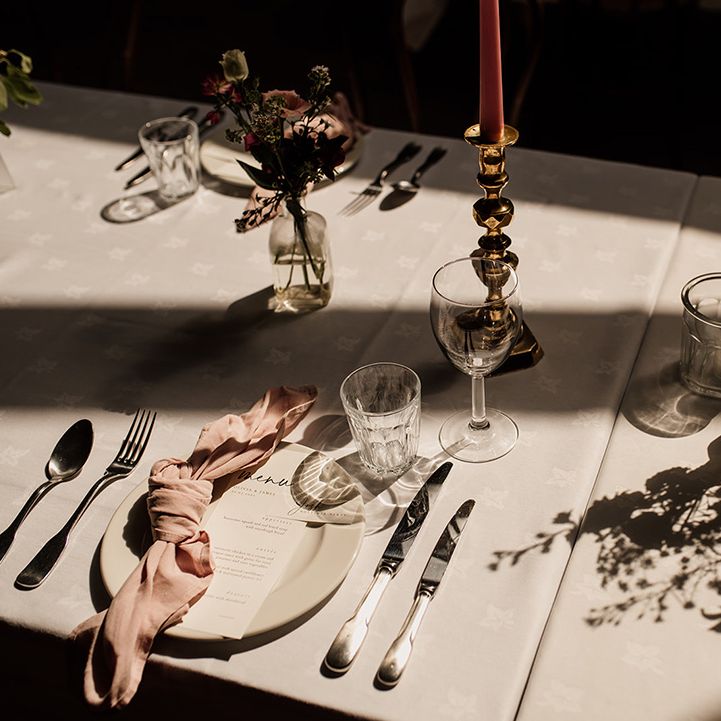Plain white plates, tablecloth and menu card with pink napkins and pink candles in gold holders