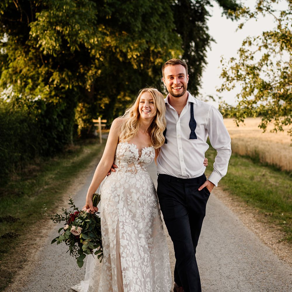 Groom walks with his arm around the bride with his bow tie undone and bride wears a strapless lace wedding dress 
