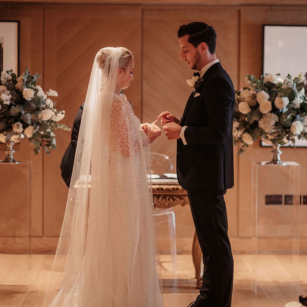 Bride and groom look down at the new wedding ring as they get married 