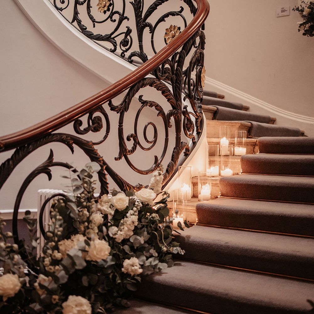 White rose and green foliage flower decoration along the staircase with candles 