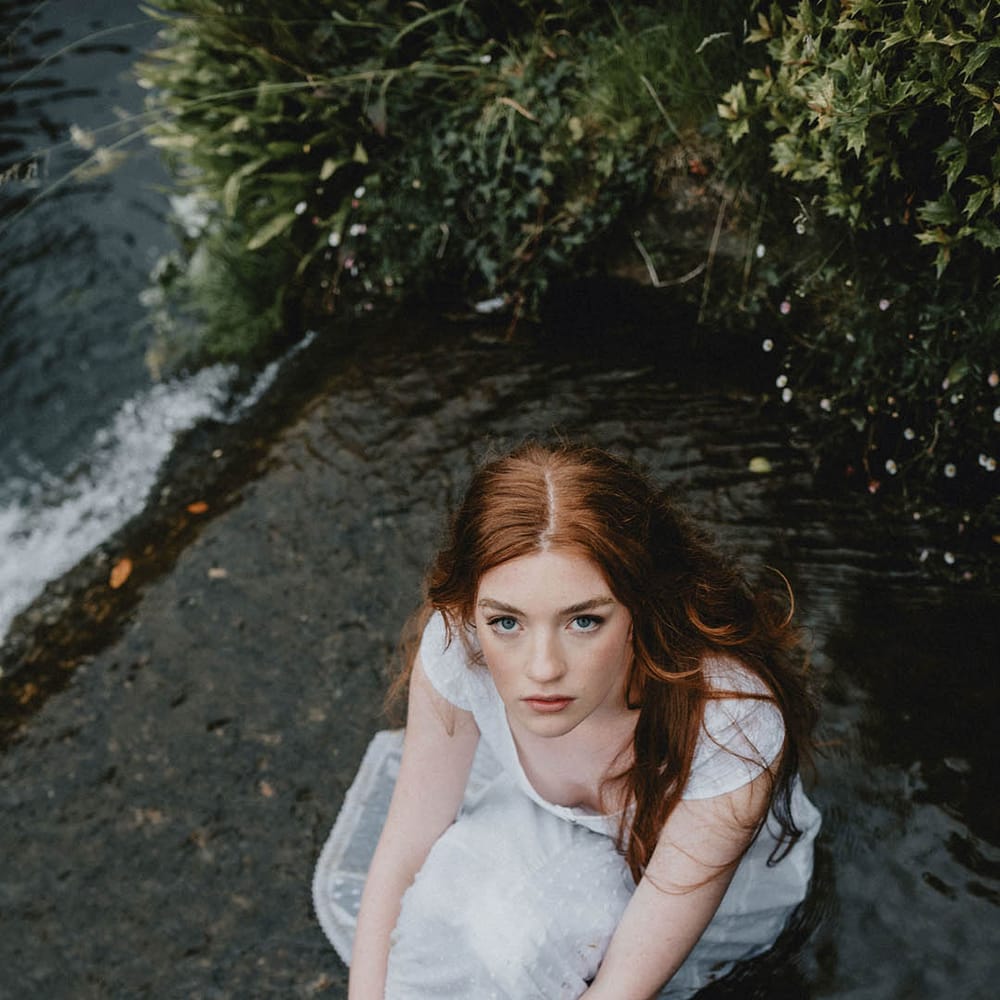 Beautiful bride with long hair and natural makeup sitting in the moat at Bishop's Palace, Wells