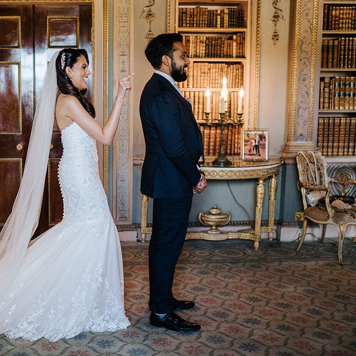 Bride wears lace fitted mermaid wedding dress with cathedral veil as she stands behind her groom for first look moment at Syon Park