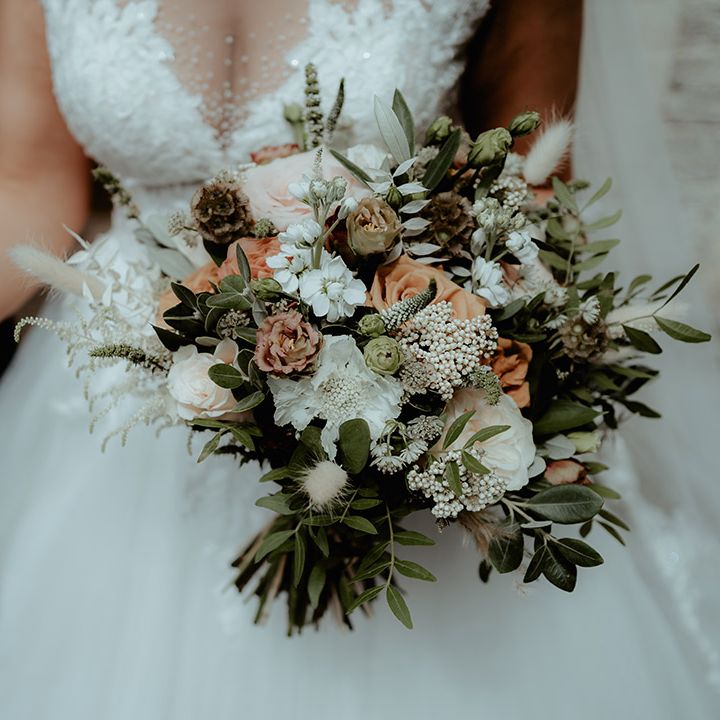 Bride holding an orange and white wedding bouquet with roses, bunny grass and baby's breath 
