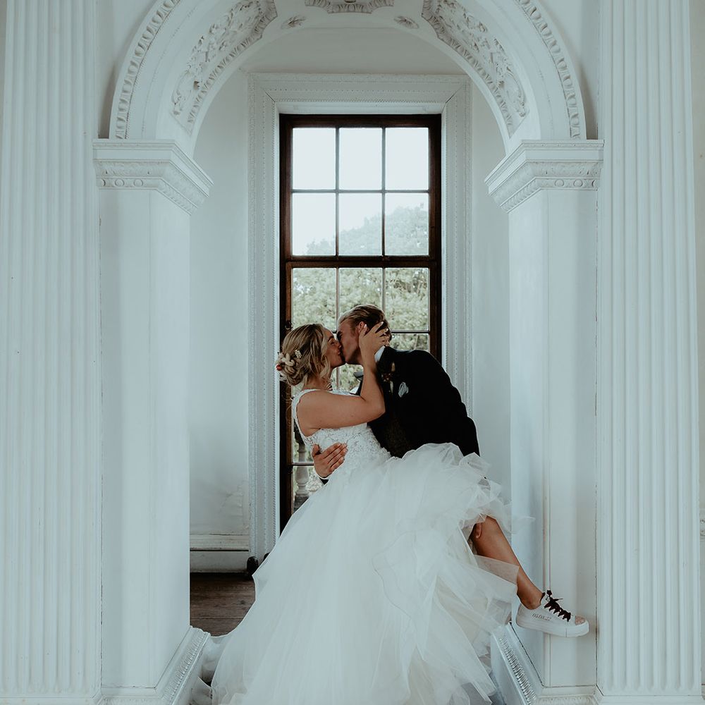 Bride wearing personalised wedding Converses kisses the groom at their wedding for the Badminton Estate