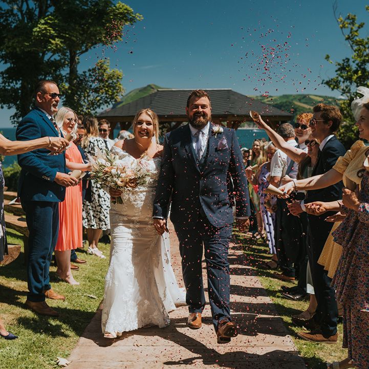 Bride & groom walk through colourful confetti after wedding ceremony outdoors 