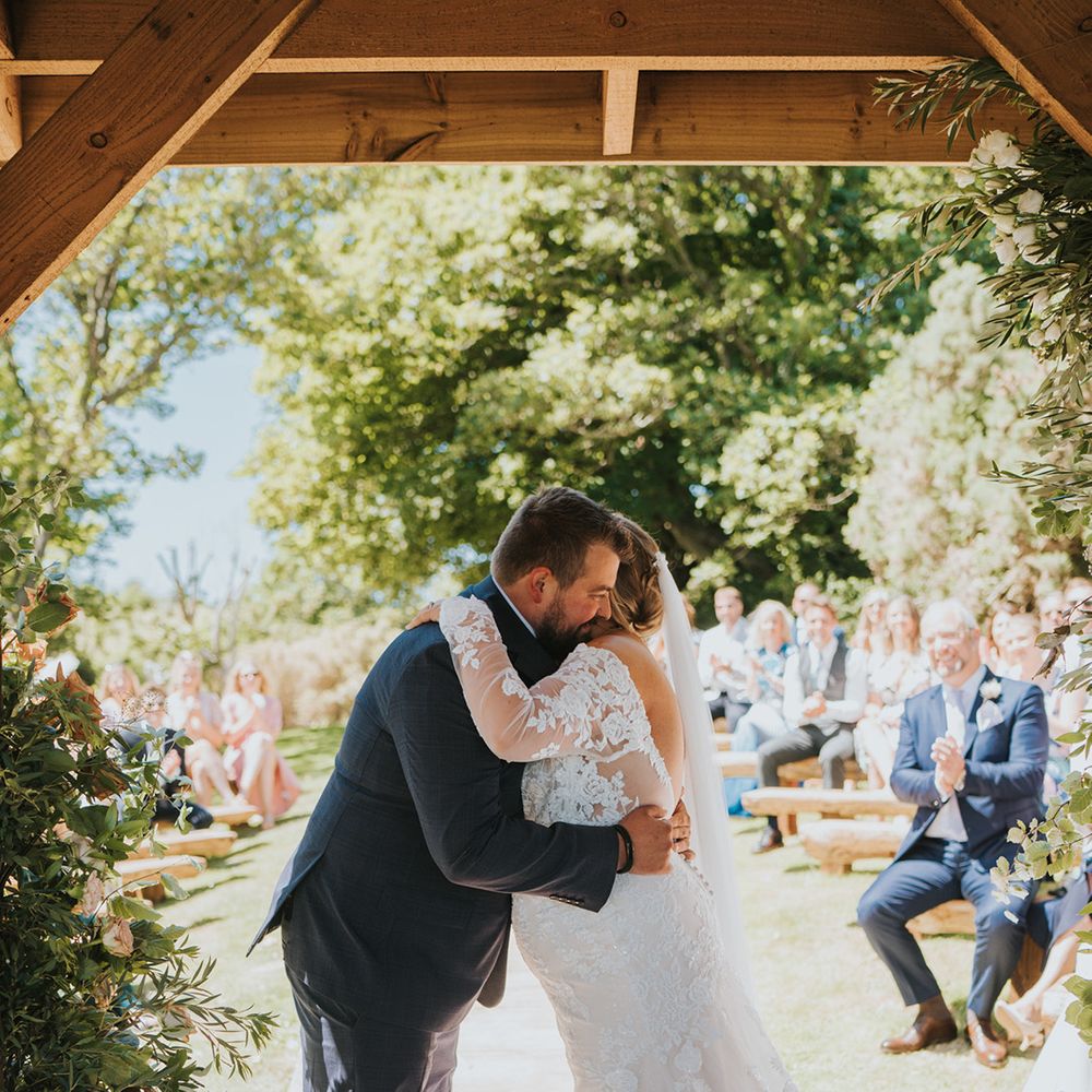 Bride in long sleeve lace wedding dress hugs her groom outdoors 