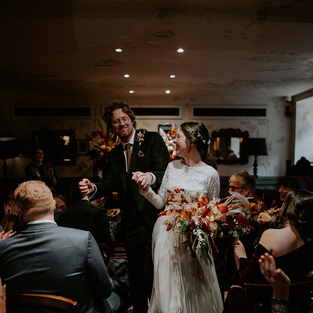 Bride in long sleeve lace vintage wedding dress and closed toe satin heels and groom in dark suit with orange tie dancing down the aisle at The Zetter Townhouse