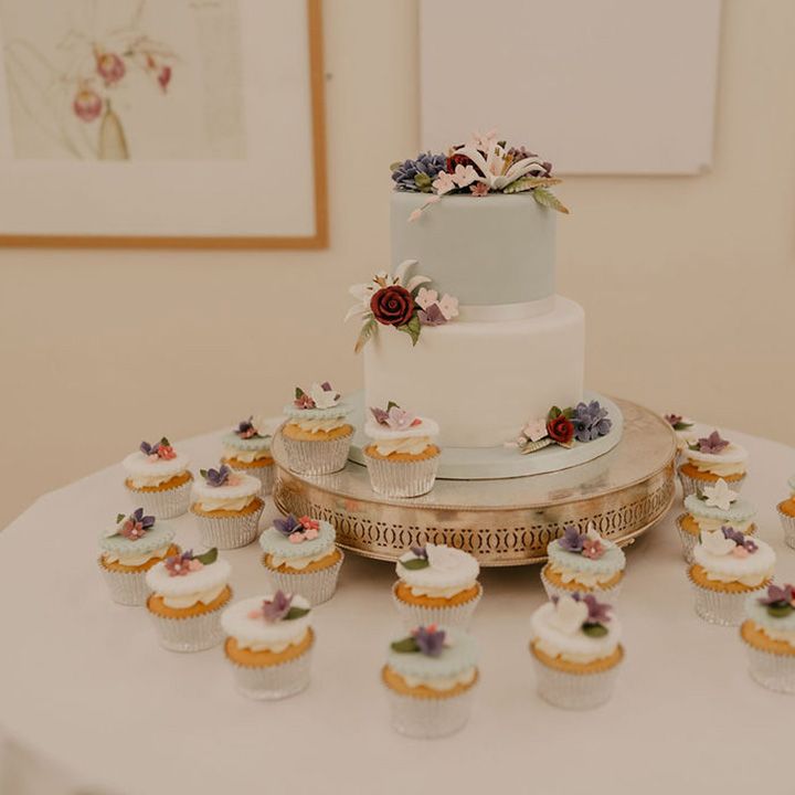 Two tier pastel wedding cake surrounded by mini pastel cupcakes finished with fondant floral design