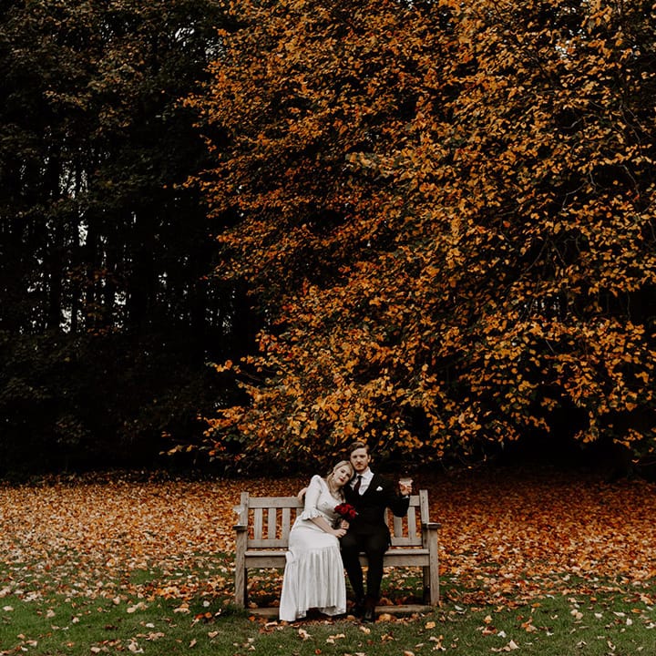 Autumnal wedding with the bride and groom sitting on a wooden bench together for their Halloween wedding 
