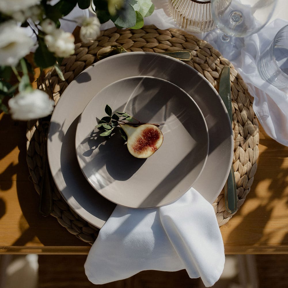 Wedding table place setting with fig, green and white floral decor, glasses and white tablecloth at private villa wedding in Greece