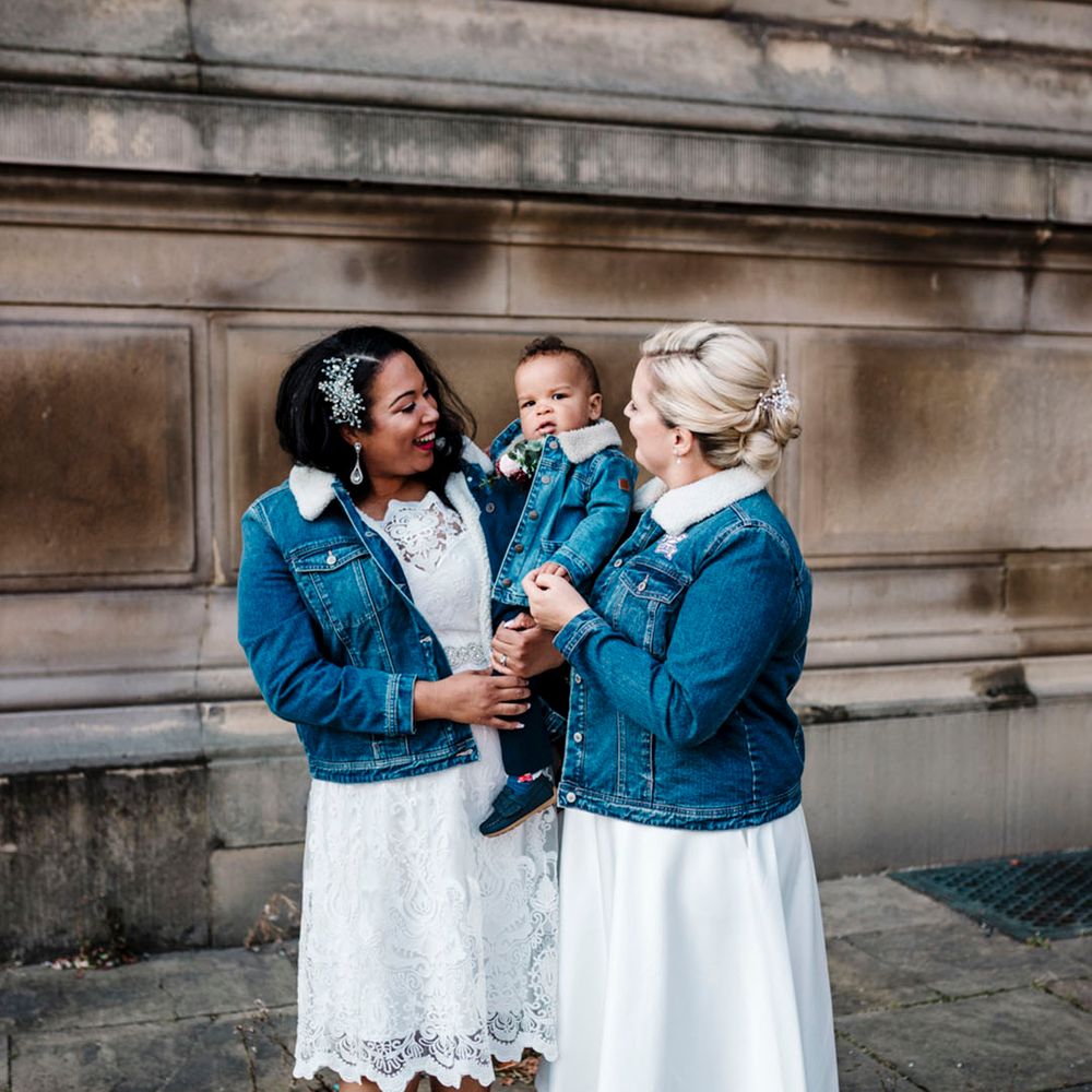 Two brides wearing dark blue denim jackets with white fur trim collars matching their little boy 