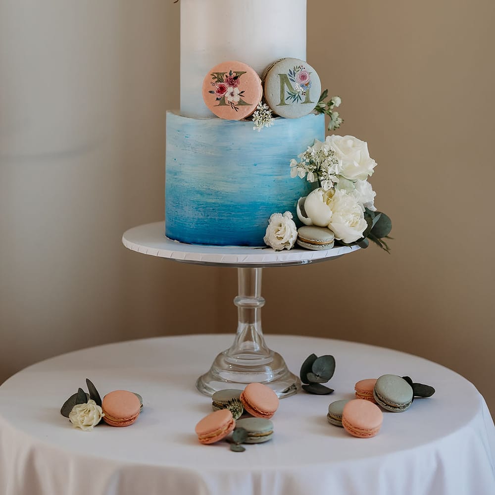 Three tier blue ombre iced wedding cake with pastel macaroons and white roses 