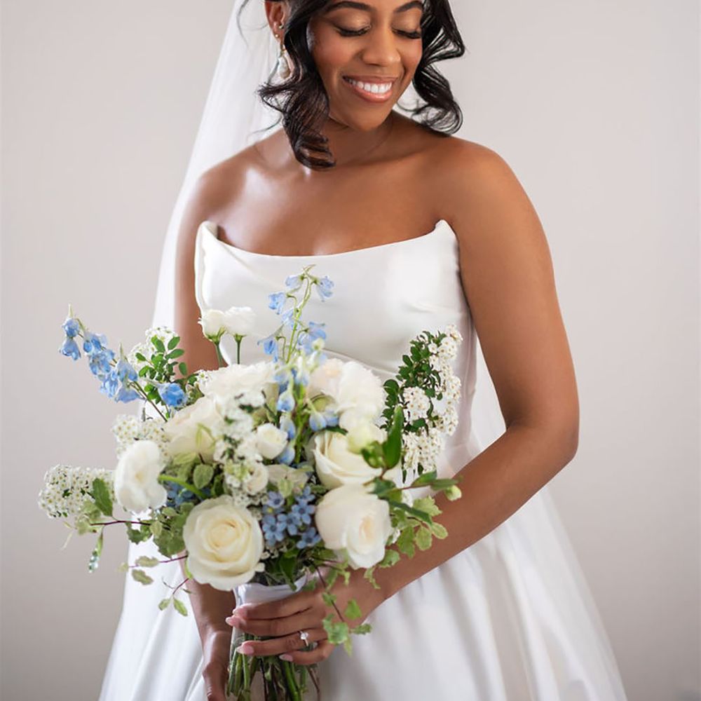 Bride holding white and blue wedding bouquet with white roses and foliage 