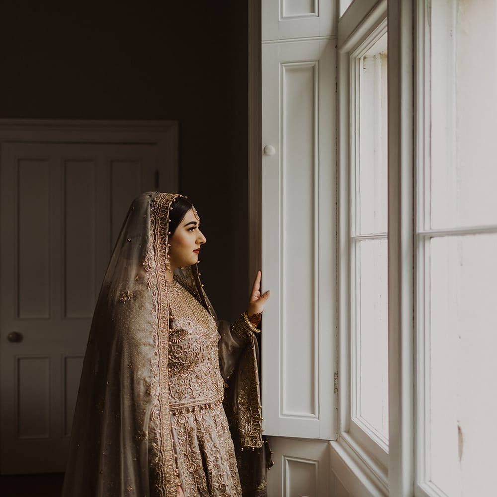 Muslim bride in a gold sari looking out of the window on her wedding day 