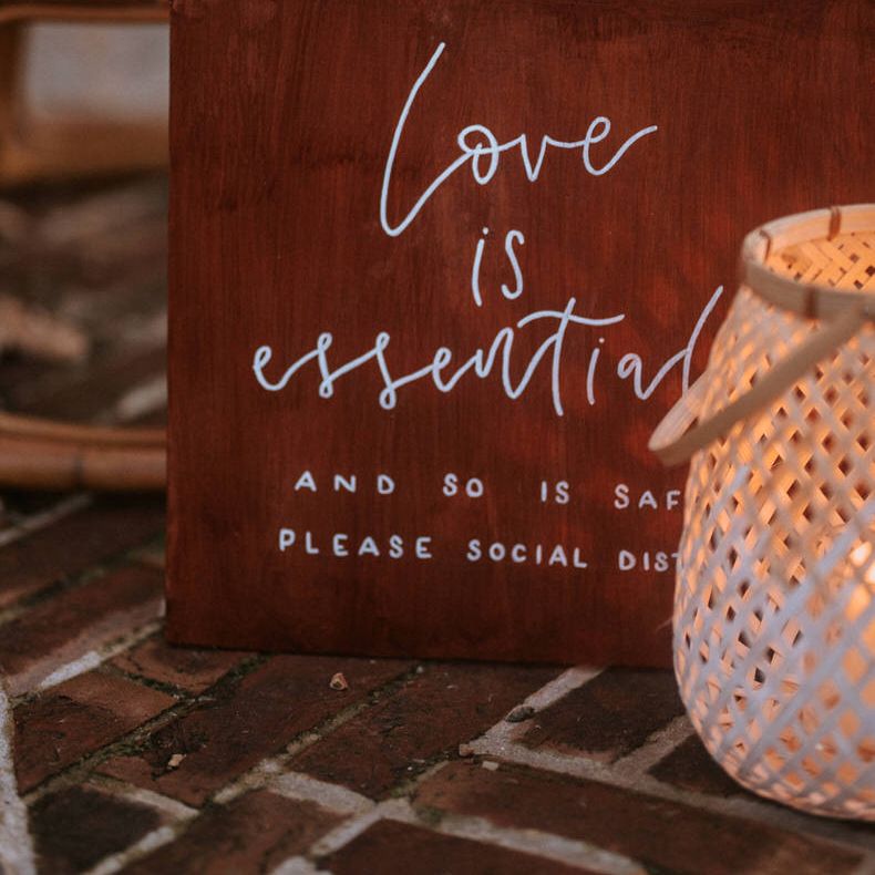 Painted board reading: Love is essential and so is safety, please social distance