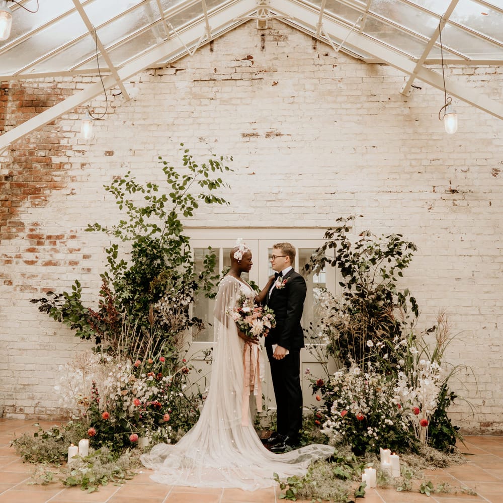 Intimate elopement wedding ceremony at Our Beautiful Glasshouse in Sussex with wildflower arrangements and bride and groom exchanging vows 