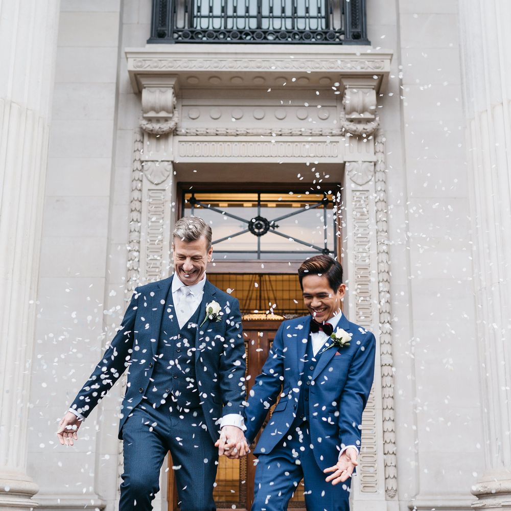 Grooms leave Old Marylebone Town Hall with blue confetti being thrown around them