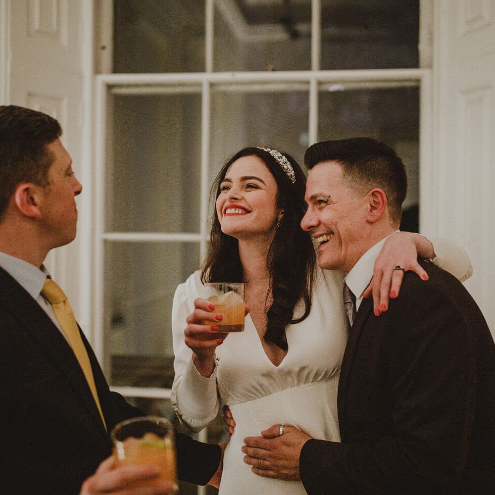 Bride hugging wedding guests smiling, holding a cocktail with peach red nail varnish